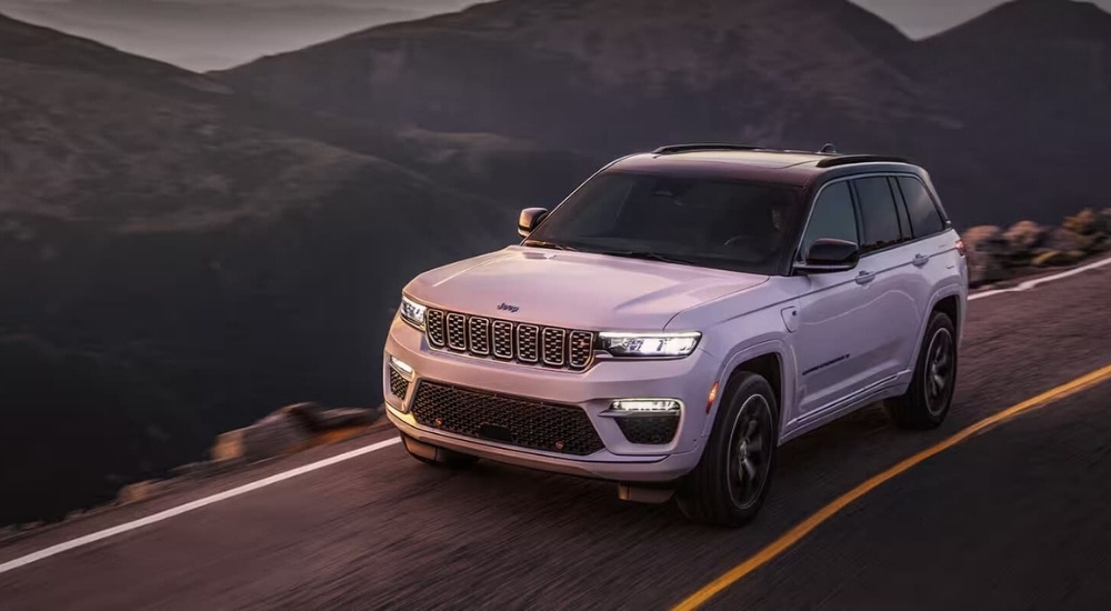 A white 2024 Jeep Grand Cherokee 4xe is shown on a mountain road after leaving a Jeep dealership.