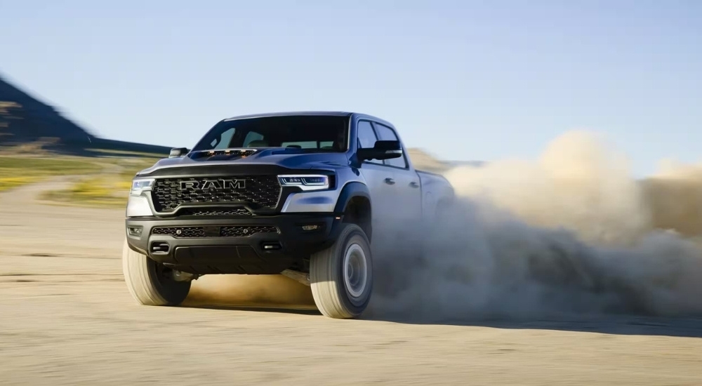 A grey 2025 Ram 1500 RHO is shown kicking up dust after leaving a Ram dealership.