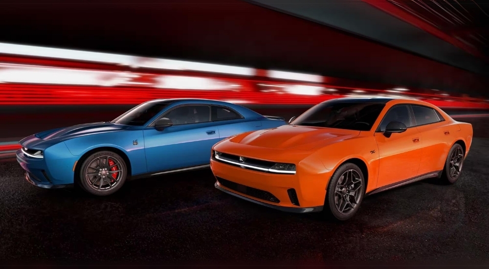 A blue 2025 Dodge Charger Scat Pack and orange Charger RT are shown driving to a Dodge dealer near Red Hook.