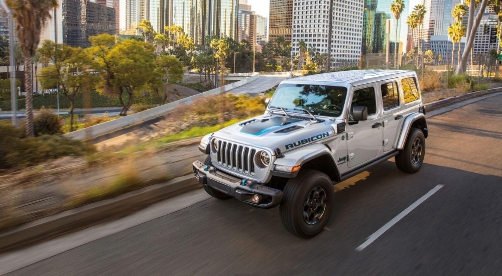 A silver 2023 Jeep Wrangler 4xe Rubicon is shown driving on a city street.