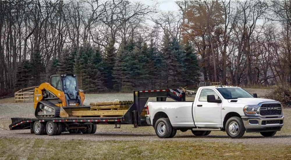 A white 2024 Ram 3500 is shown towing lumber and construction equipment.