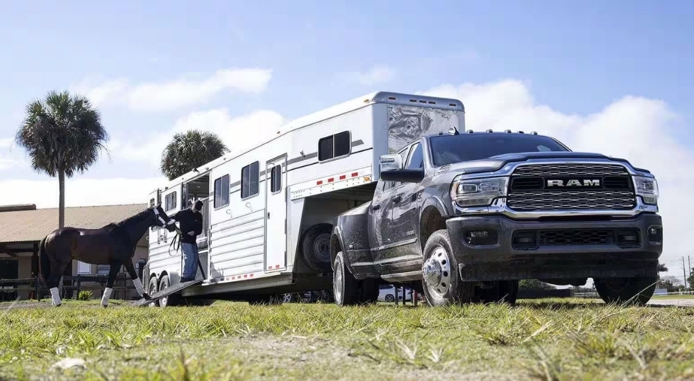 A grey 2024 Ram 3500 is shown towing a horse trailer.