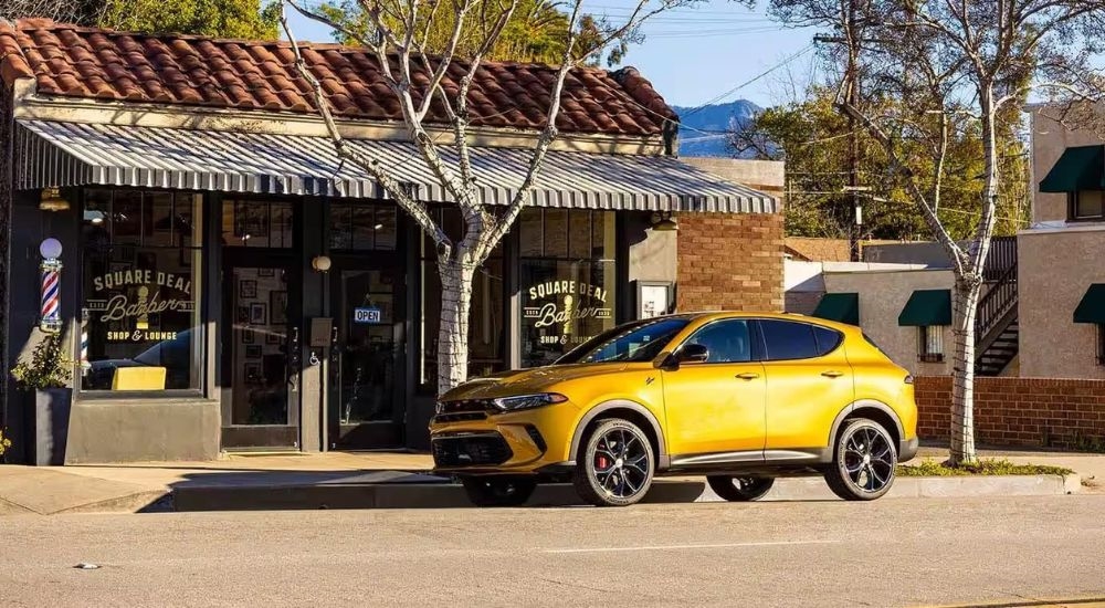 A gold 2024 Dodge Hornet is shown parked near a barber shop after visiting a Dodge dealer.