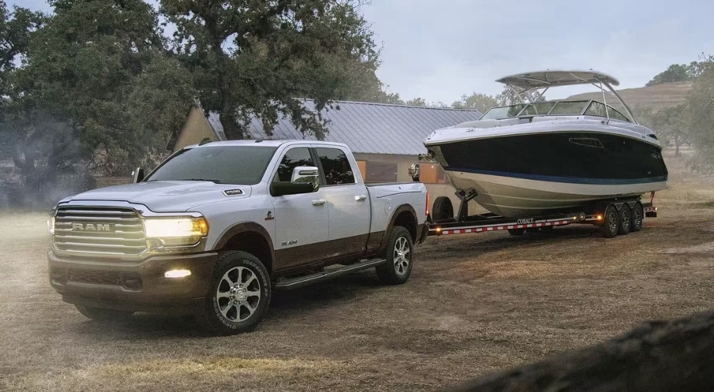 A white 2024 Ram 2500 is shown towing a boat on a dirt lot.