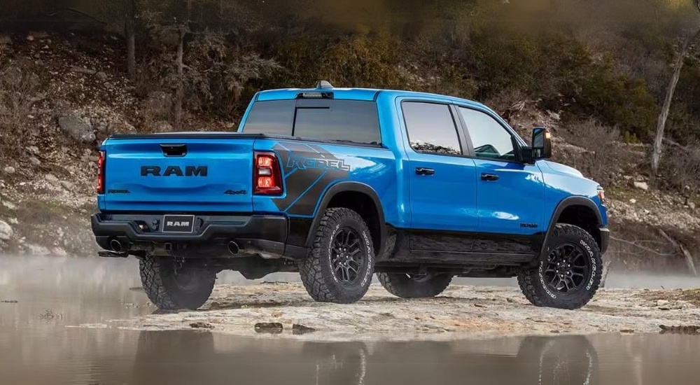 A blue 2025 Ram 1500 Rebel is shown from the rear parked off-road.