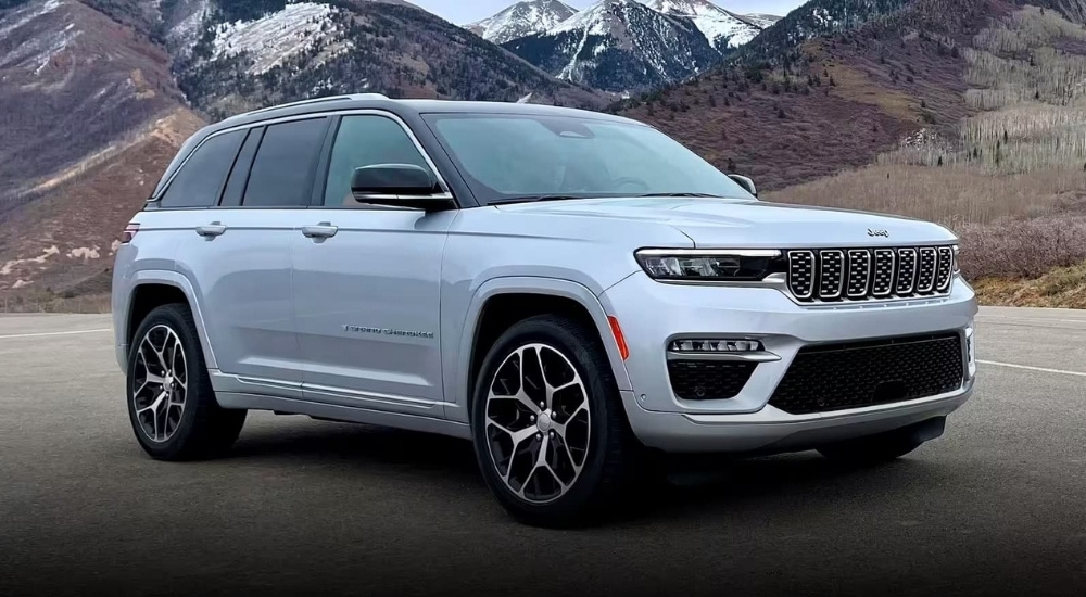 A silver 2024 Jeep Grand Cherokee is shown parked near snow-covered mountain.