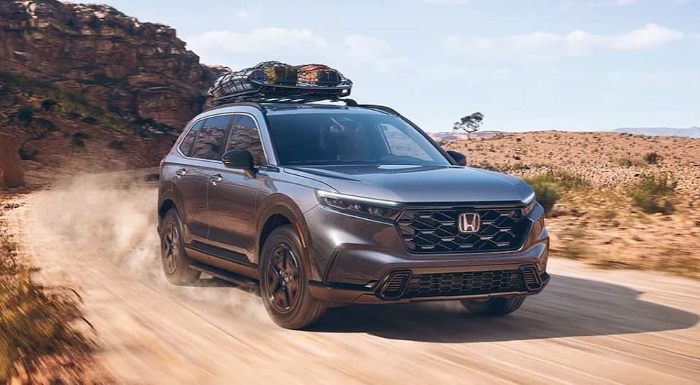 A grey 2023 Honda CR-V Sport Hybrid driving around a bend on a dirt road.