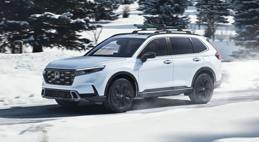 A white 2023 Honda CR-V Sport Touring Hybrid angled left and driving on a snowy road.