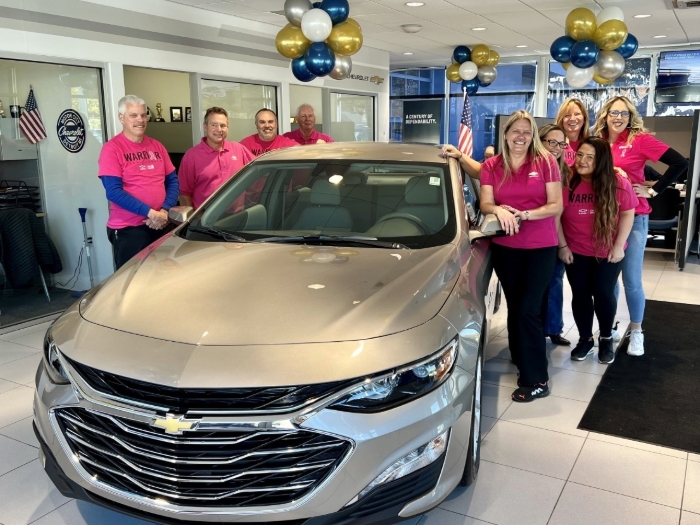 People are shown surrounding a tan Chevy Malibu.