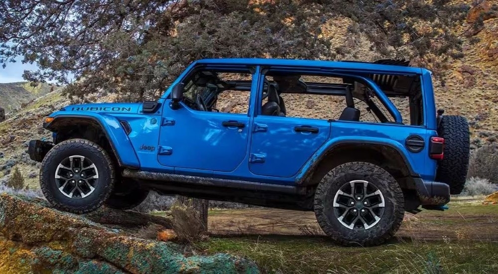 A side angle view of a blue 2024 Jeep Wrangler 4xe Rubicon parked off-road.