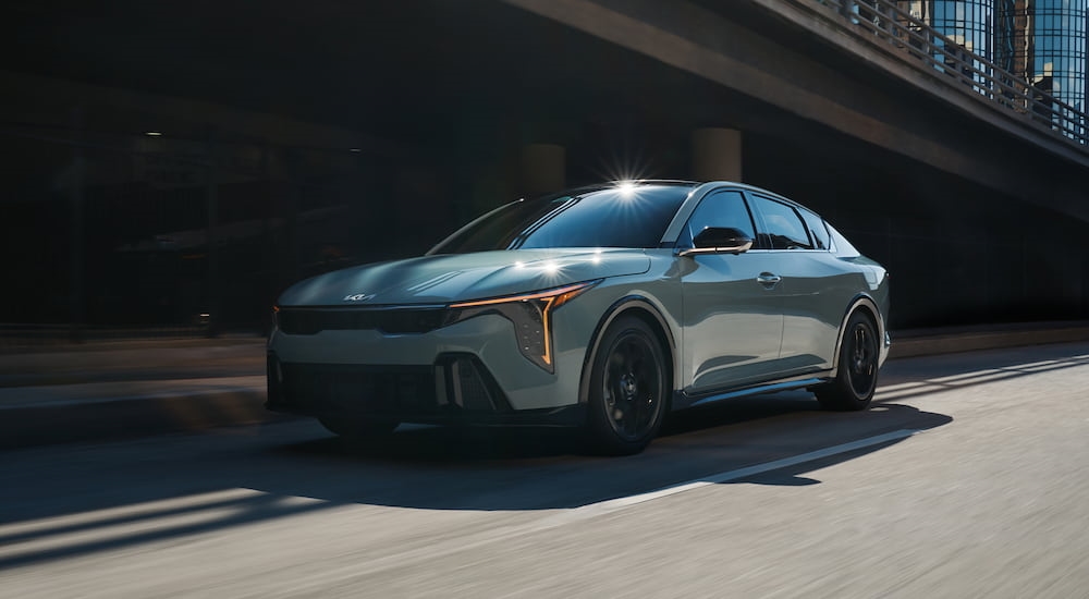 A teal 2025 Kia K4 driving by a bridge in a city.