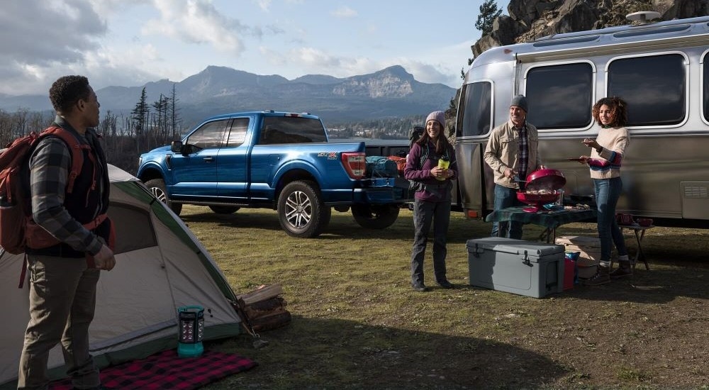 A group of people standing by a blue 2024 Ford F-150 STX parked off-road on a field with an Airstream cooler.