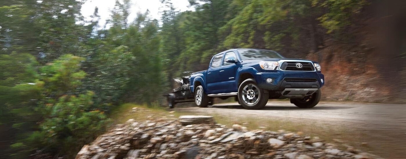 A blue 2015 Toyota Tacoma for sale is shown towing an ATV.