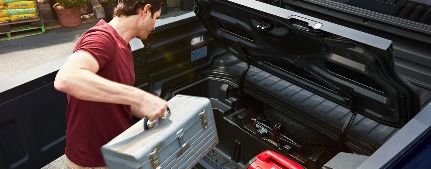 A person is shown stowing a tool box in the bed of a grey 2025 Honda Ridgeline.