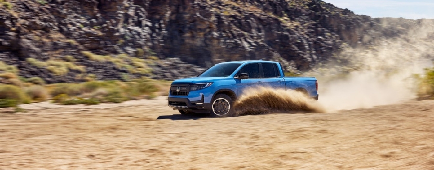 A blue 2025 Honda Ridgeline HPD+ is shown kicking up dust.