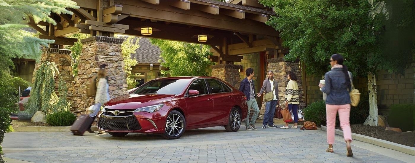 A red 2016 Toyota Camry for sale is shown in front of a hotel.