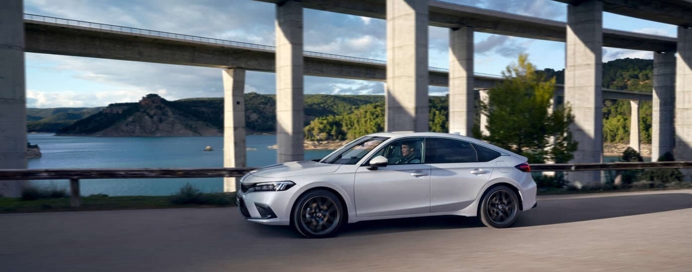 A white 2024 Honda Civic is shown from the side driving past bridges.