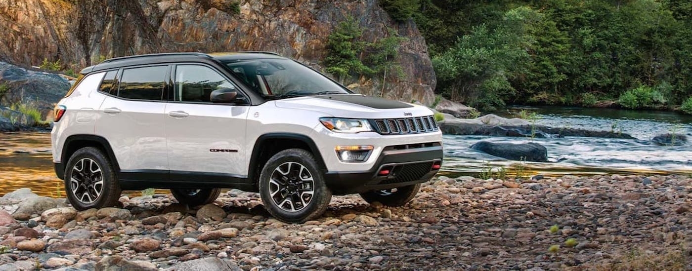 Side angle view of a white 2020 Jeep Compass Trailhawk parked on a river shore.