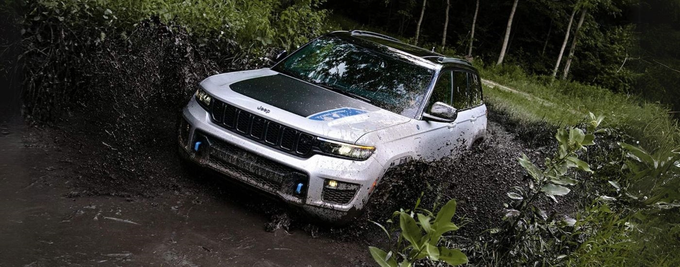 A white 2022 Jeep Grand Cherokee 4xe driving through a mud puddle.