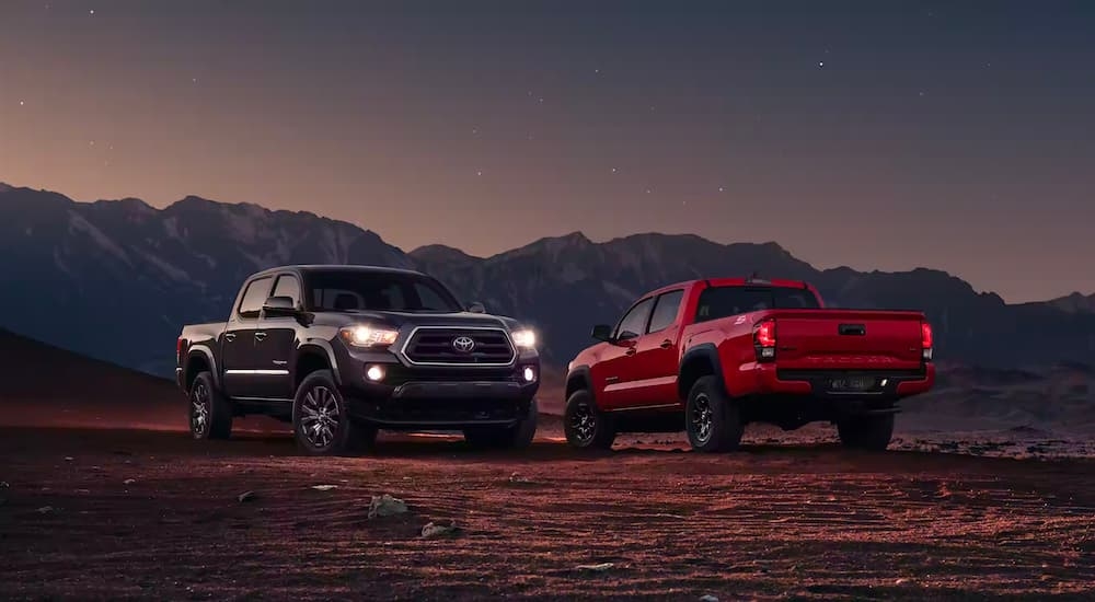 A black 2023 Toyota Tacoma SR5 parked off-road and angled right next to the red 2023 Toyota Tacoma SR5.