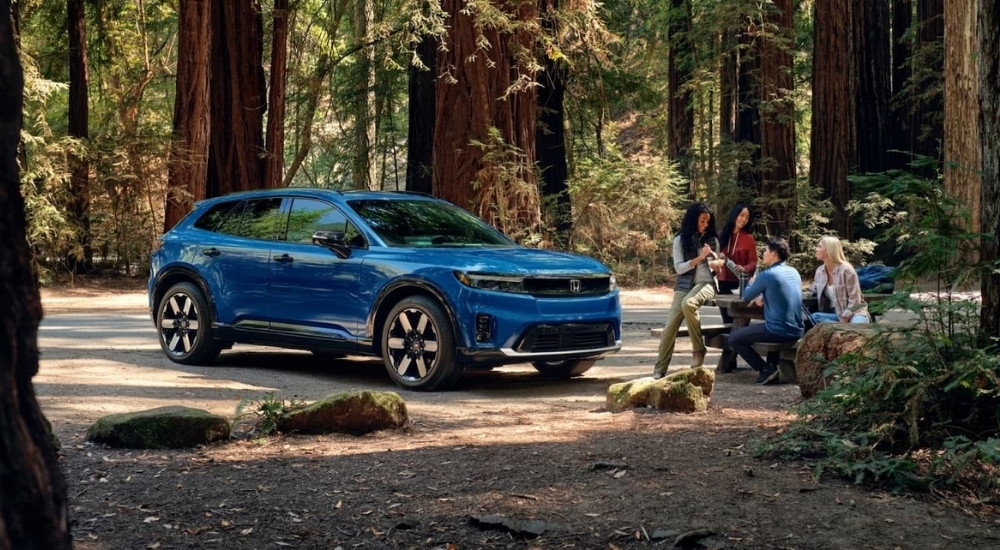 A blue 2024 Honda Prologue Elite is shown near people on a picnic table.