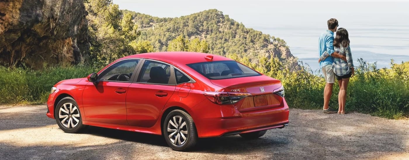 Rear view of a couple standing next to a red 2024 Honda Civic LX.