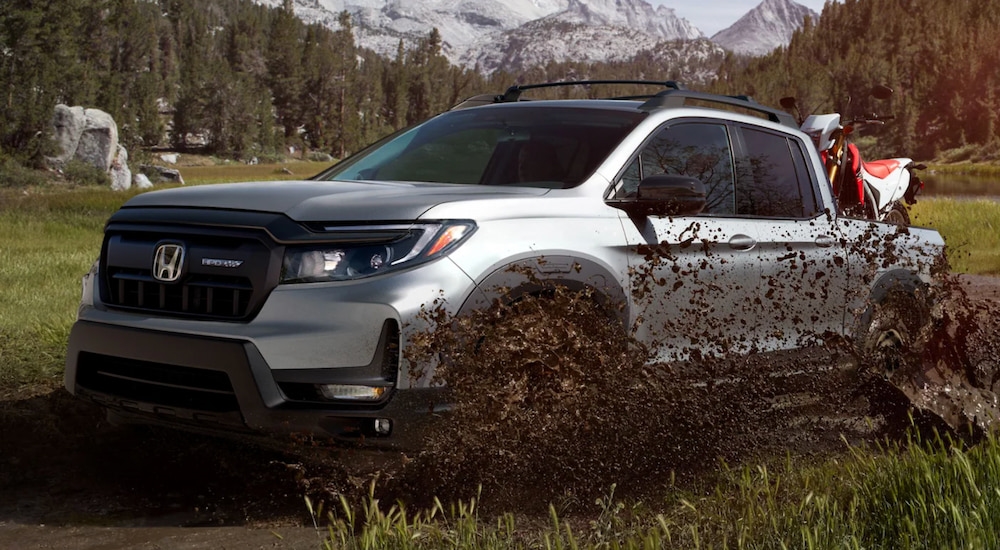 A silver 2025 Honda Ridgeline Sport splashing through mud while off-roading.