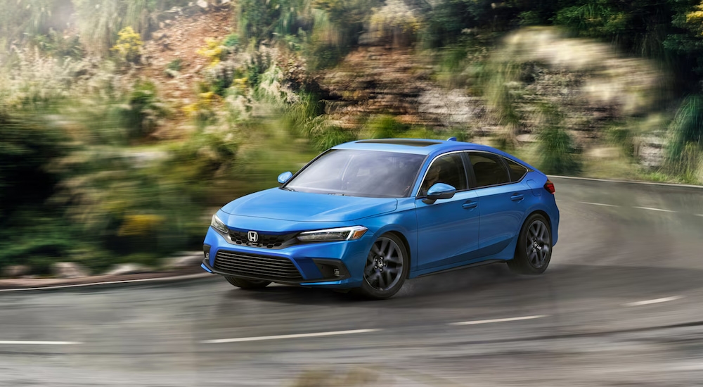 A blue 2025 Honda Civic Hatchback Sport Touring driving around a curve.