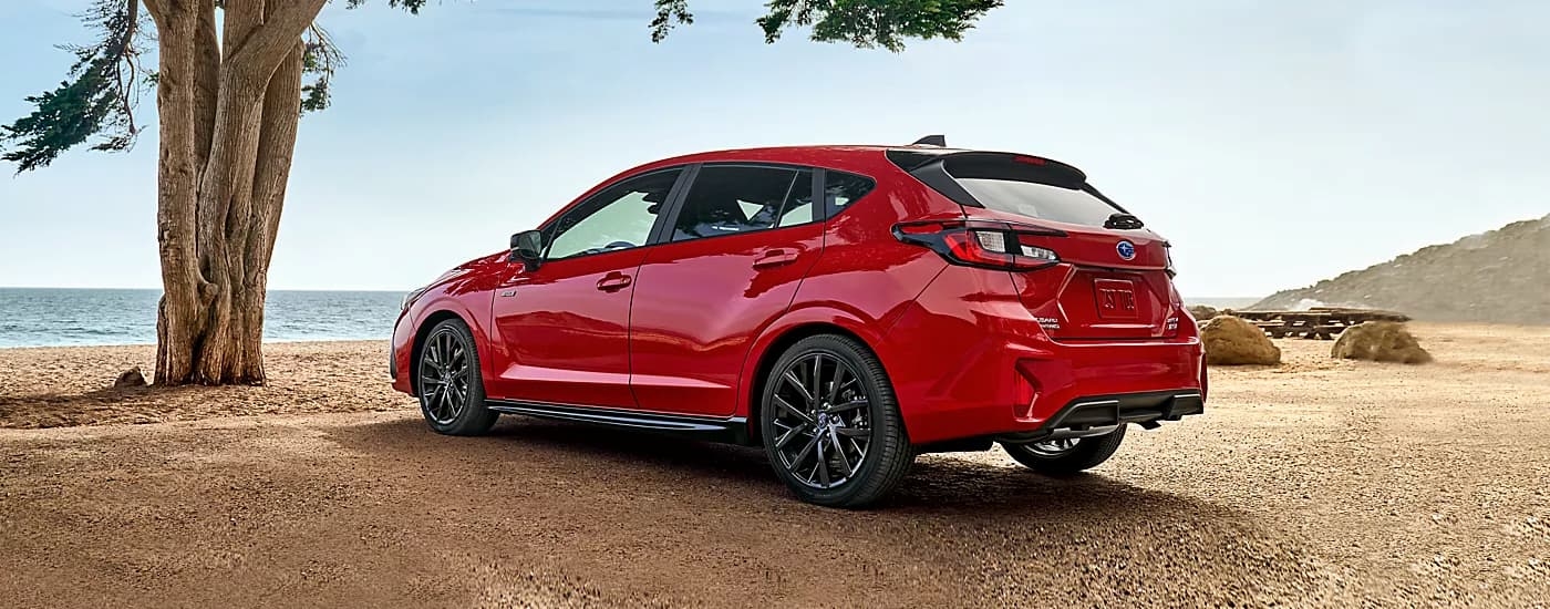 Rear angle view of a red 2024 Subaru Impreza parked on a beach.