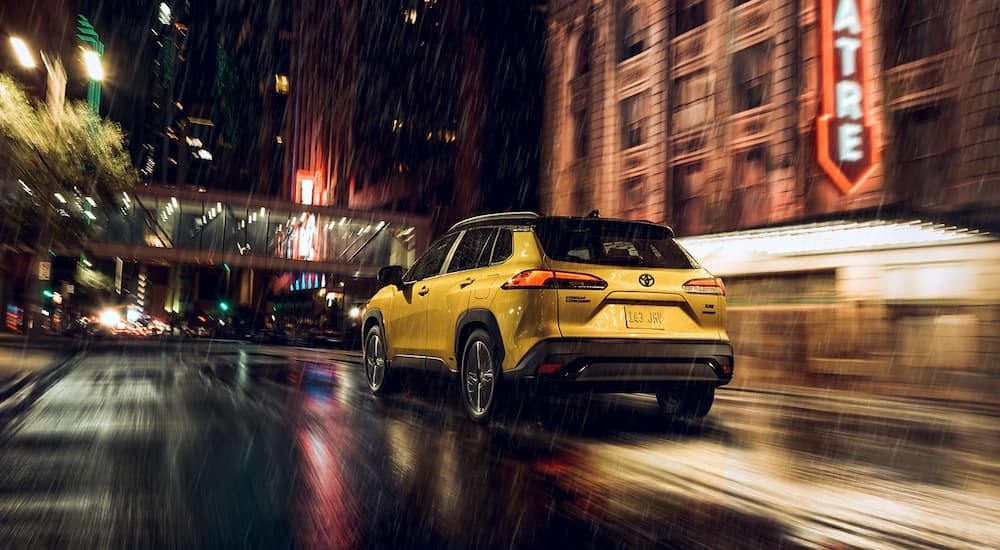 Side angle view of a yellow 2024 Toyota Corolla Cross Hybrid driving through a rainy city.