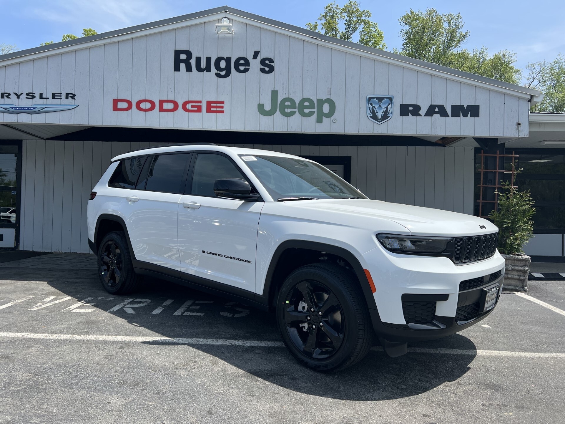 A white Jeep Grand Cherokee L Altitude is shown parked in front of Ruge's CDJR.