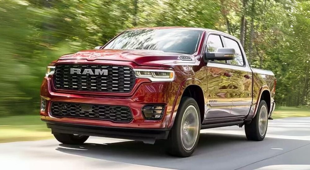 A red 2025 Ram 1500 is shown driving on an tree-lined road.