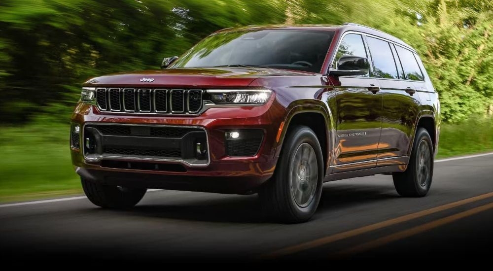 A maroon 2023 Jeep Grand Cherokee is shown driving on a tree-lined road.