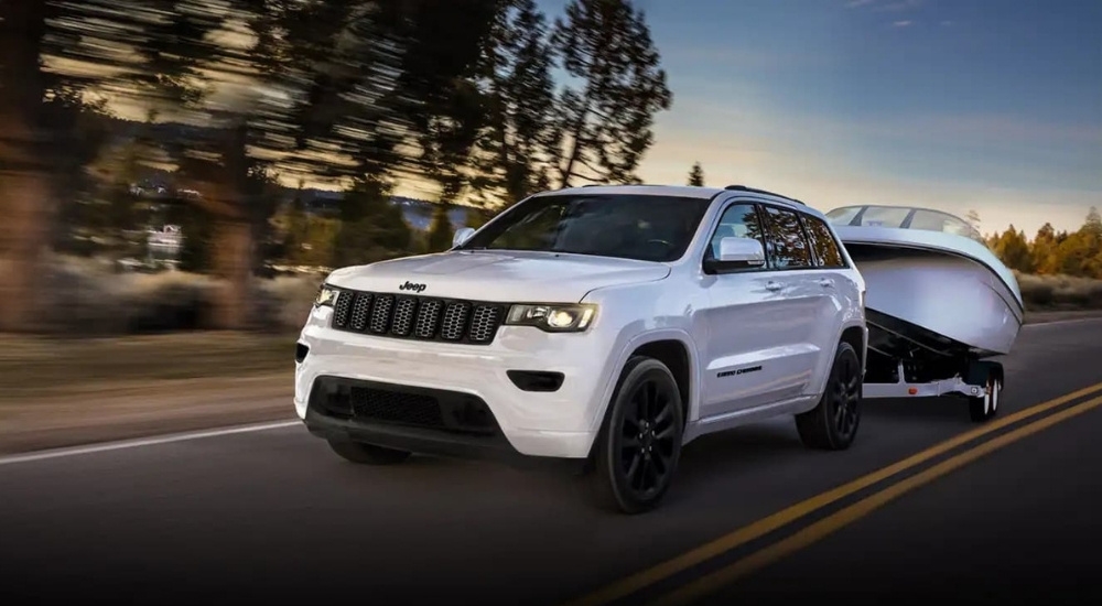 A white 2021 Jeep Grand Cherokee is shown towing a boat.