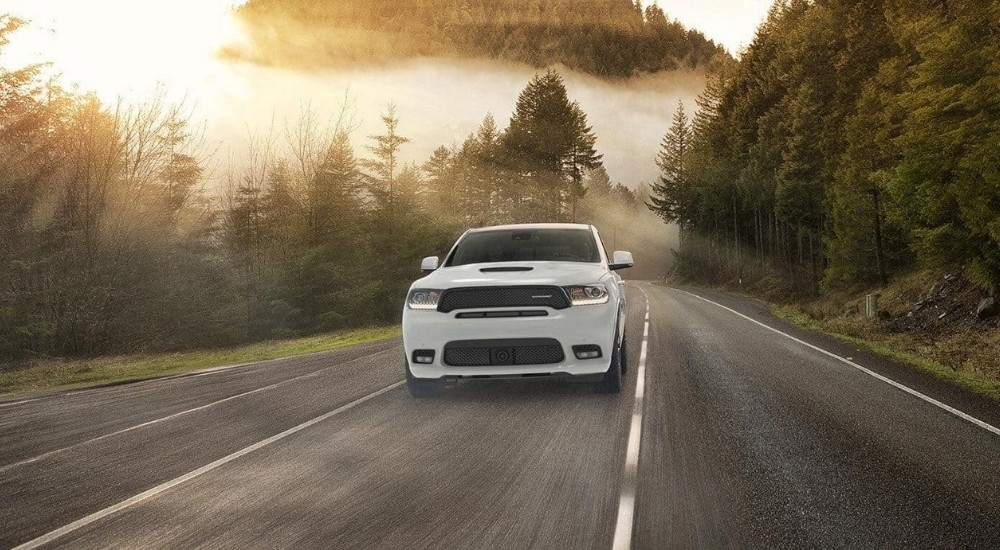 A white 2020 Dodge Durnago RT is shown driving on a tree-lined road.