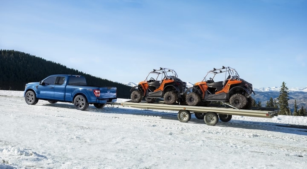 A blue 2022 Ford F-150 STX is shown towing ATVs.