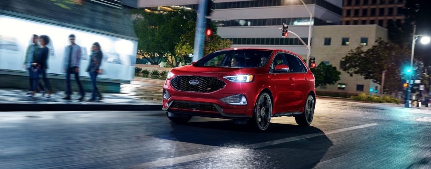 A red 2022 Ford Edge ST driving through a city at night from a used SUV dealer.