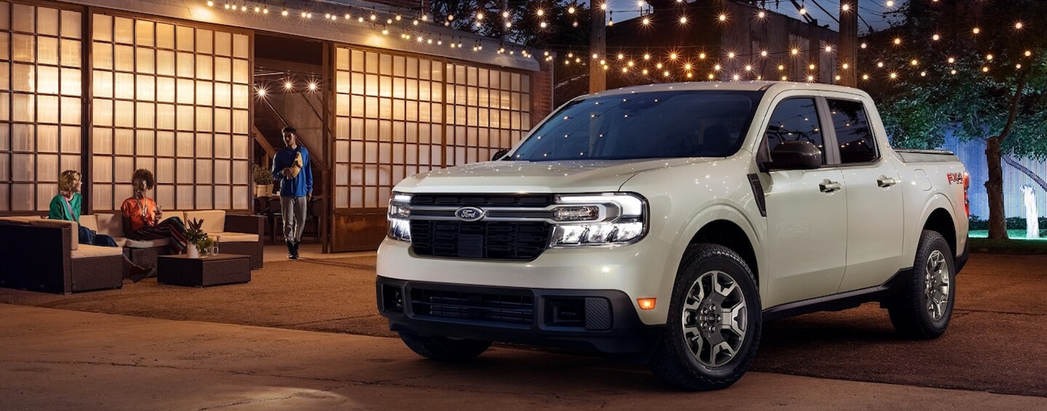 An off-white 2024 Ford Maverick LARIAT parked under patio lights at night.