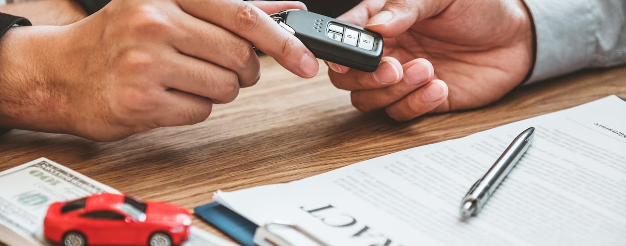 A car salesman is shown handing a key to a customer.