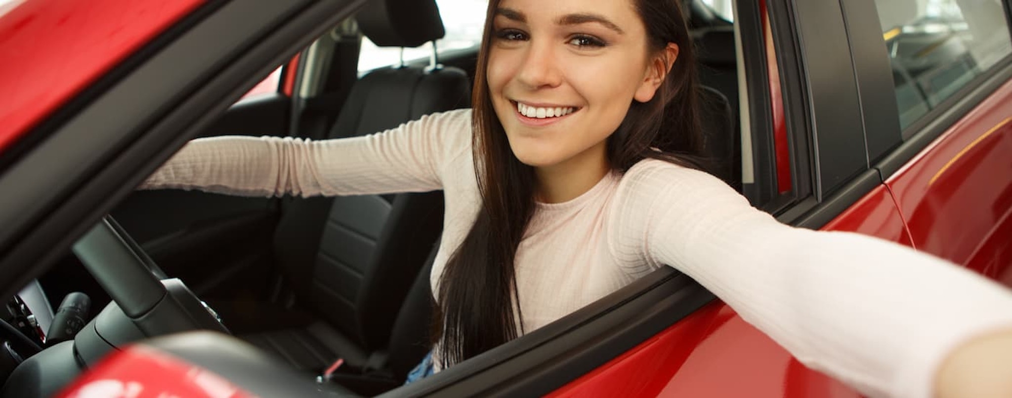 A woman is shown sitting in the front seat of a red vehicle after asking about subprime auto loans near Keene, NH.