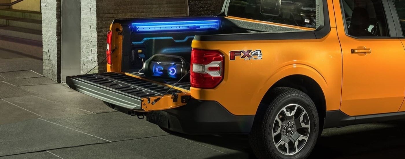 A boombox and accent lighting are shown in the bed of a yellow 2024 Ford Maverick FX4.