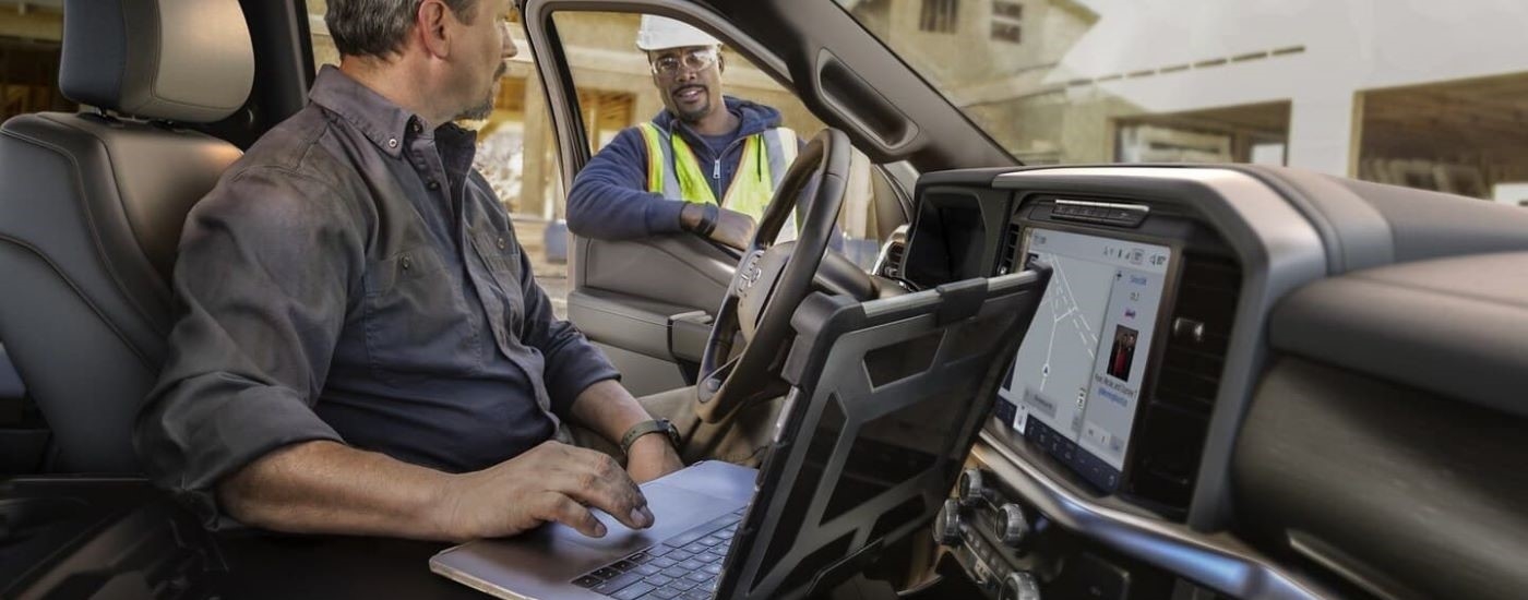 A person sitting in a 2024 Ford F-150 Lariat is shown using a laptop.