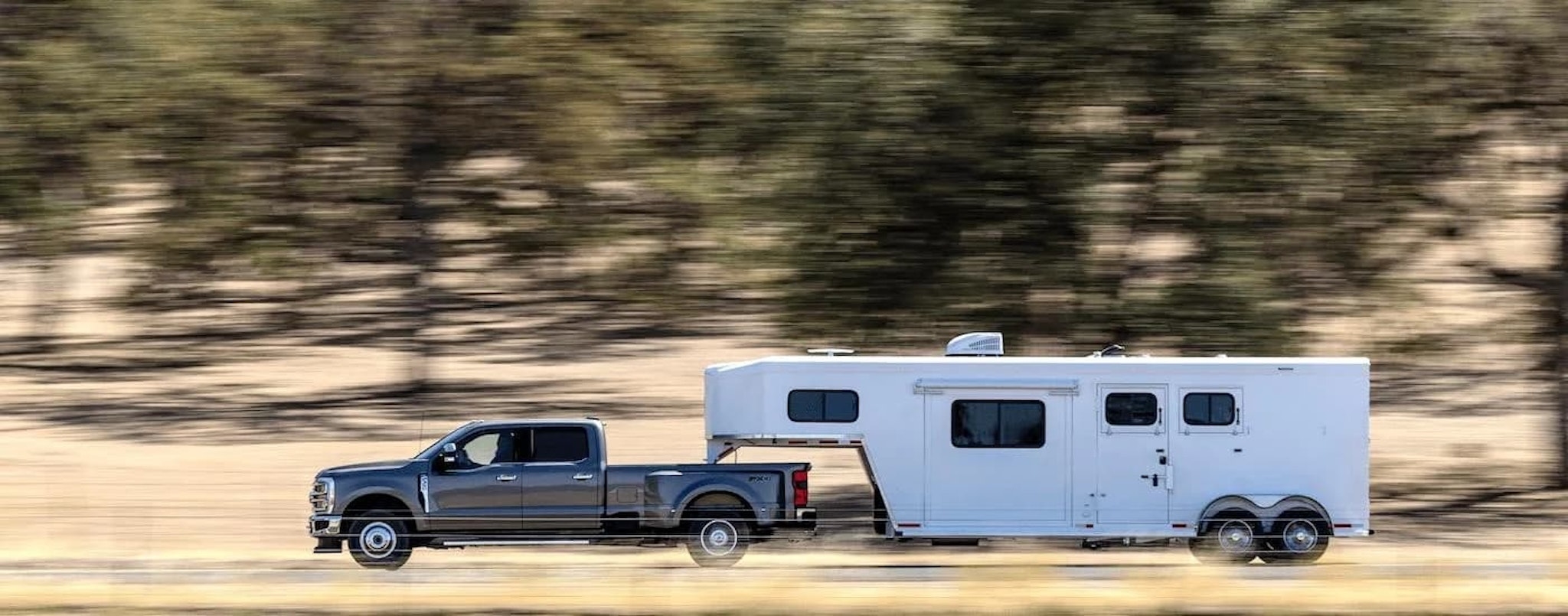 A grey 2023 Ford F-350 is shown from the side while towing a camper after leaving a used Ford truck dealer.