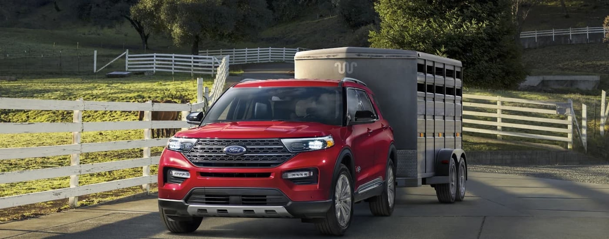 A red 2023 Ford Explorer is shown towing a horse trailer through a farm.