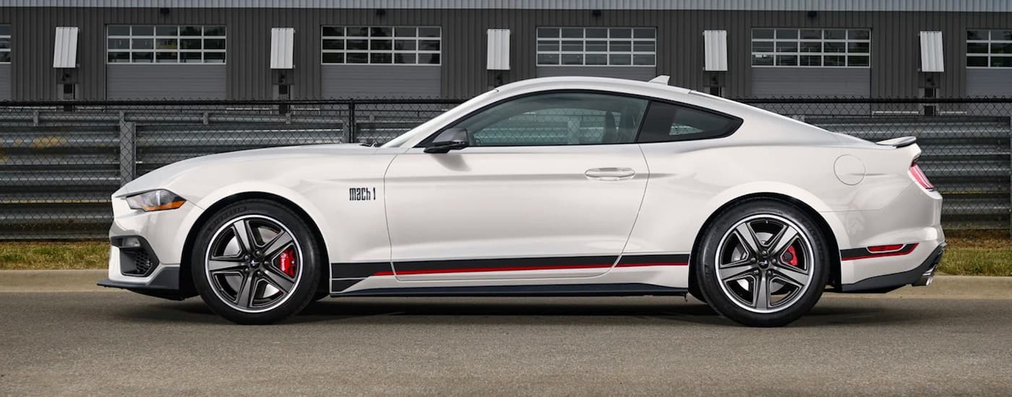 A white 2022 Ford Mustang Mach 1 is shown from the side in front of a warehouse.