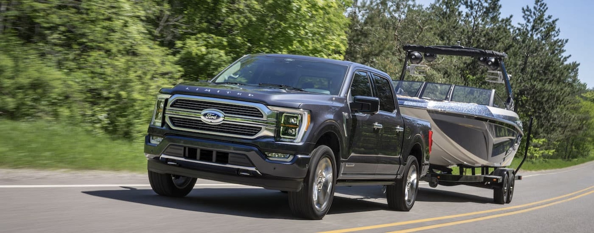 A grey 2022 Ford F-150 Limited is shown from the front while towing a boat after leaving a dealer that has used trucks for sale.