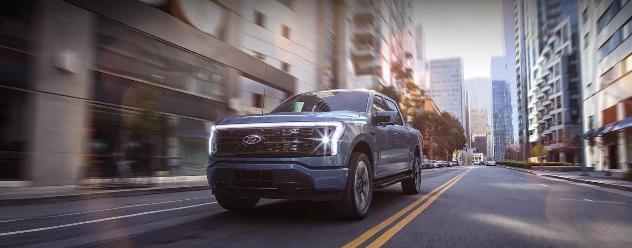 A blue 2024 Ford F-150 Lightning is shown driving on a city street.