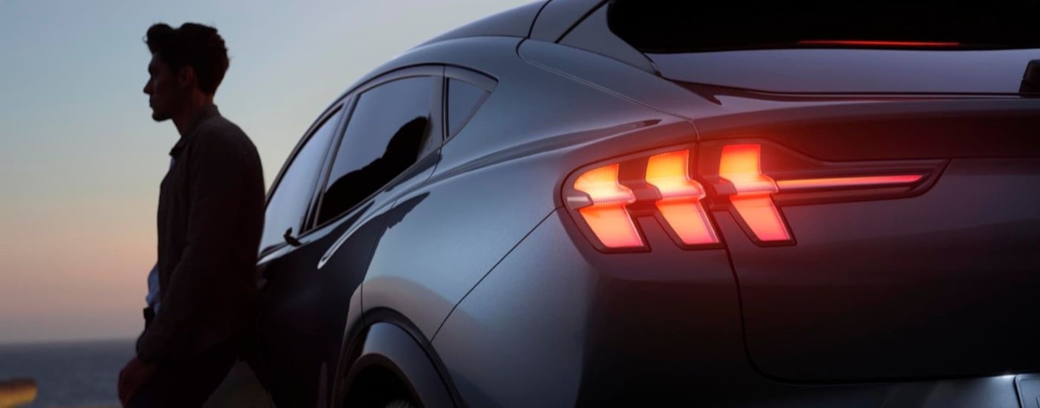 A person is shown leaning against a grey 2023 Ford Mustang Mach-E.