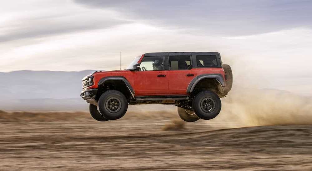 An orange 2024 Ford Bronco Raptor is shown from the side while jumping through the air after leaving a Ford Bronco dealer.