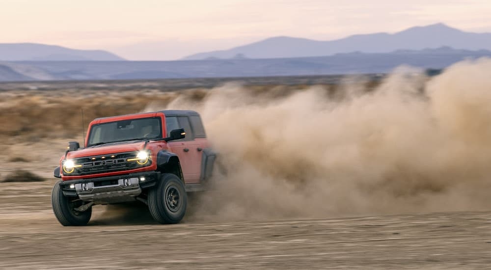 An orange 2024 Ford Bronco Raptor is shown from the front while drifting through sand.
